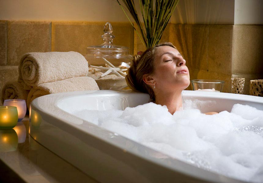 Woman relaxing in tub treatment with bubbles and candles. 