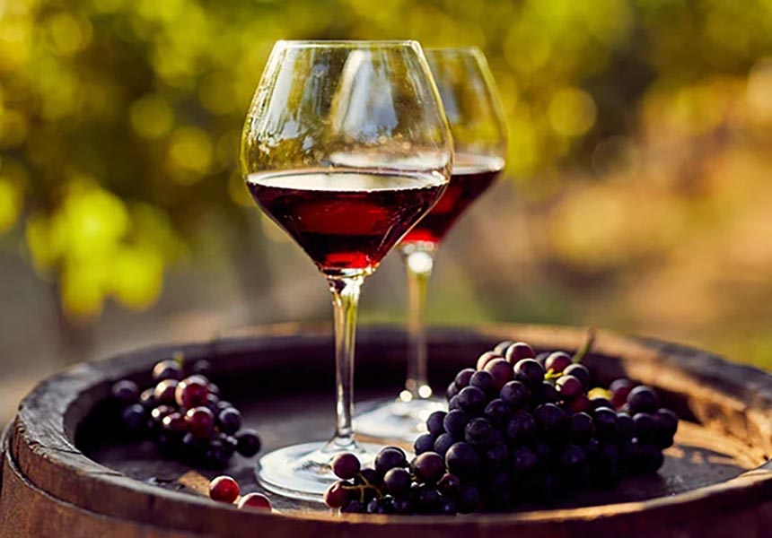 Red wine and grapes set up on a wine barrel outdoors.