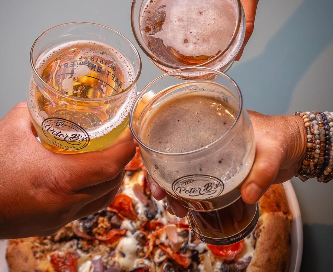 A group cheers with beer and pizza.