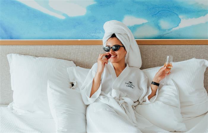 Woman in a hotel bet drinking champagne and eating a chocolate strawberry