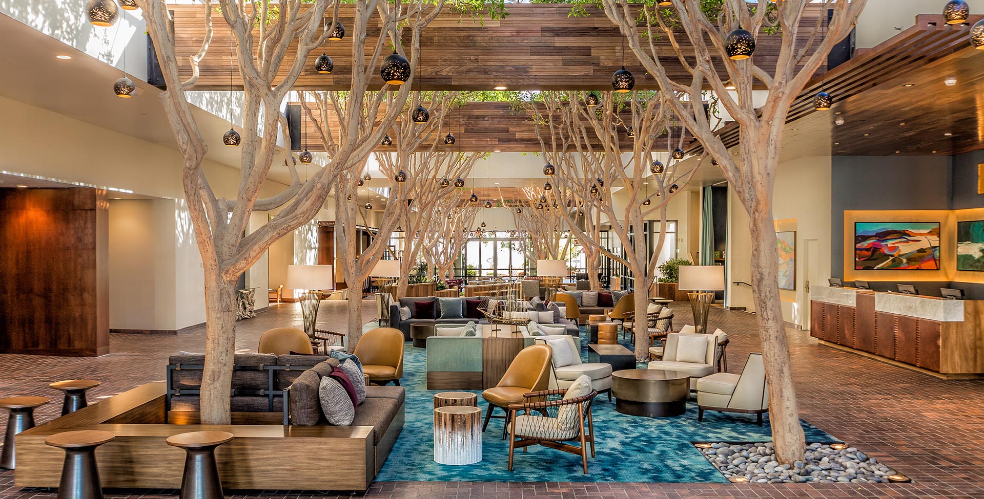 A spacious lobby with trees growing through the ceiling, surrounded by seating areas and decorated with artwork.