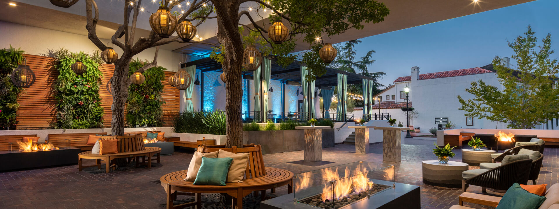 A stylish outdoor lounge area with seating, fire pits, and trees.